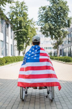 back view of veteran in wheelchair, wrapped in usa flag on city alley clipart