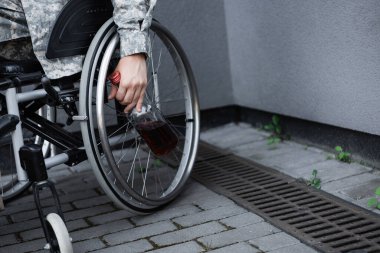 Tekerlekli sandalyede oturan bir şişe viskisi olan engelli askerin kısmi görüntüsü