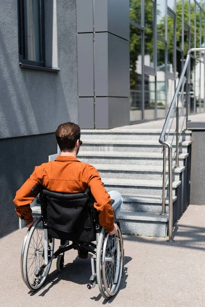 在设有楼梯的建筑物附近轮椅上的年轻残疾人士的背景 — 图库照片