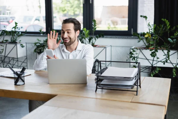 オフィスのノートパソコンでビデオ通話中に手を振っている陽気な障害者のビジネスマン — ストック写真