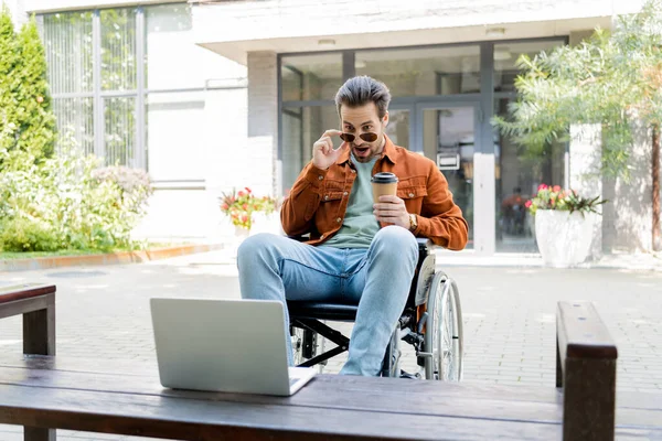 Surprised Disabled Man Taking Sunglasses While Looking Laptop Outdoors — Stock Photo, Image