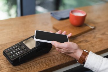 Kafede akıllı telefonla ödeme yapan bir adamın kısmi görüntüsü 