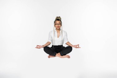 african american businesswoman with closed eyes levitating during meditation in lotus pose isolated on white clipart