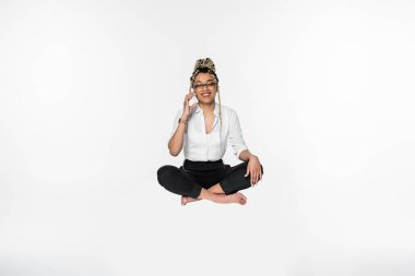 barefoot african american businesswoman talking on mobile phone while levitating in lotus pose isolated on white clipart