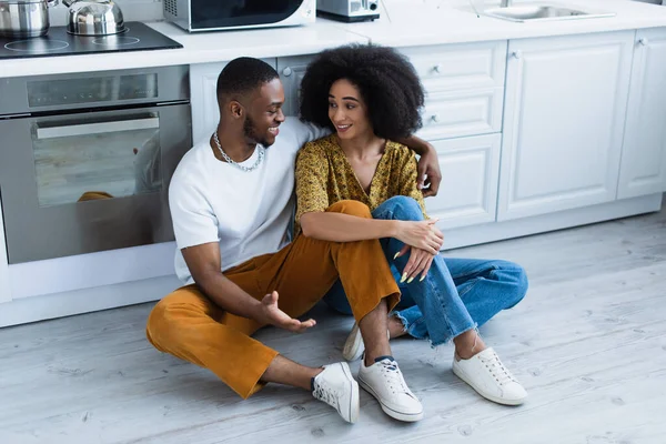 アフリカ系アメリカ人のカップルがキッチンで床で話して笑顔 — ストック写真