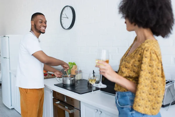 Sorrindo Homem Americano Africano Cozinhar Perto Namorada Borrada Com Vinho — Fotografia de Stock