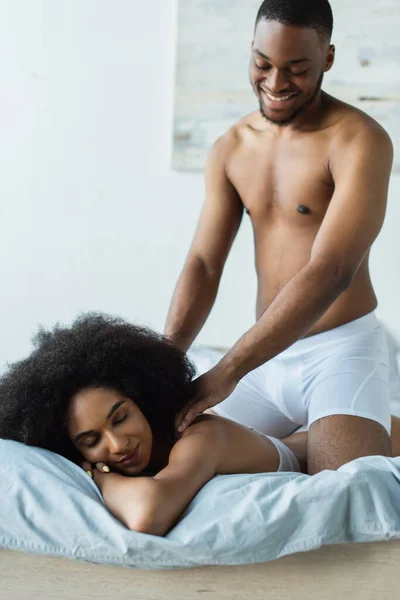 Glimlachen Afrikaanse Amerikaanse Man Masseren Schouders Van Sexy Vriendin Bed — Stockfoto