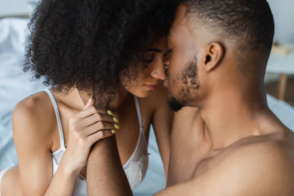 African american man kissing sensual girlfriend in bra on bed