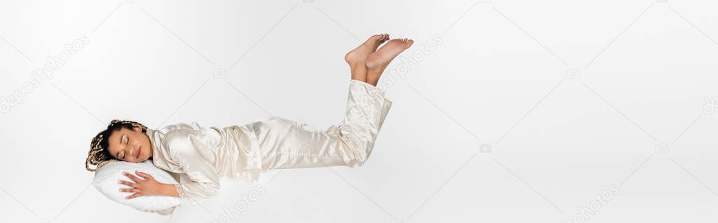 african american woman sleeping on pillow while levitating isolated on white, banner