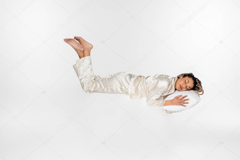 young african american woman in silk pajamas levitating in dream isolated on white