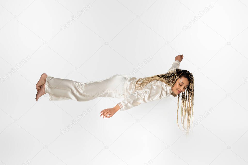 barefoot african american woman in silk pajamas sleeping in levitation isolated on white