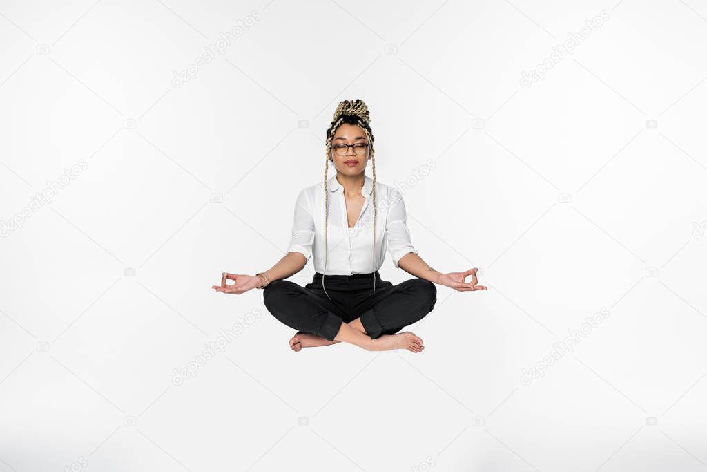 african american businesswoman with closed eyes levitating during meditation in lotus pose isolated on white