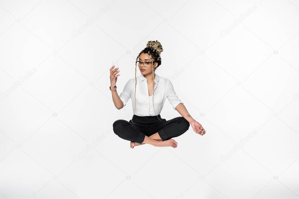 barefoot african american businesswoman with smartphone levitating in lotus pose isolated on white