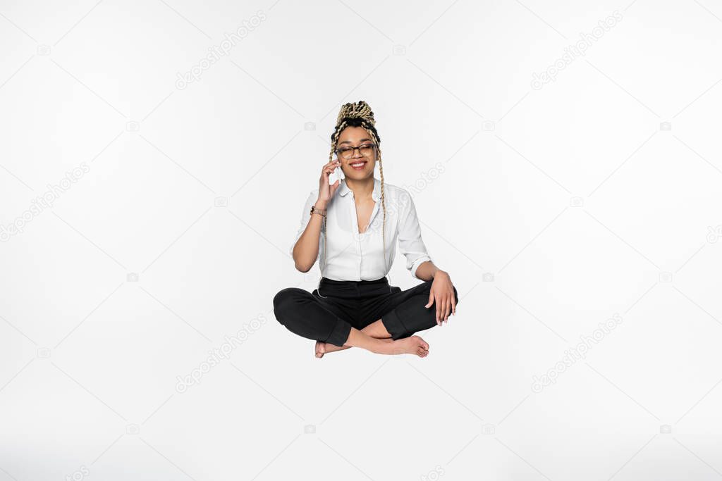 barefoot african american businesswoman talking on mobile phone while levitating in lotus pose isolated on white