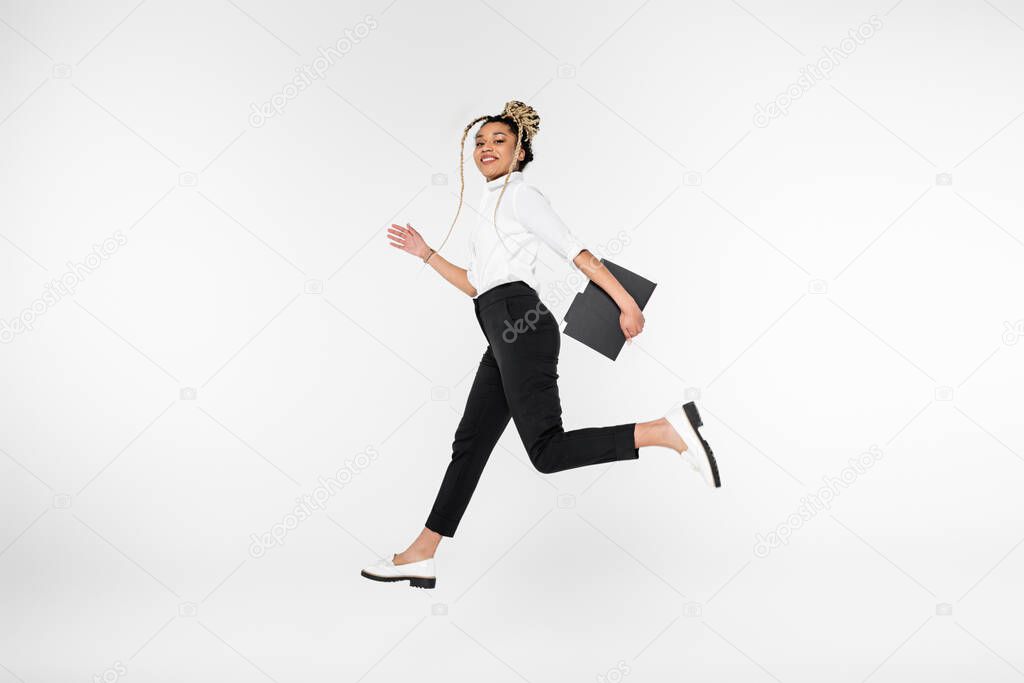 joyful african american businesswoman smiling at camera while running in levitation isolated on white