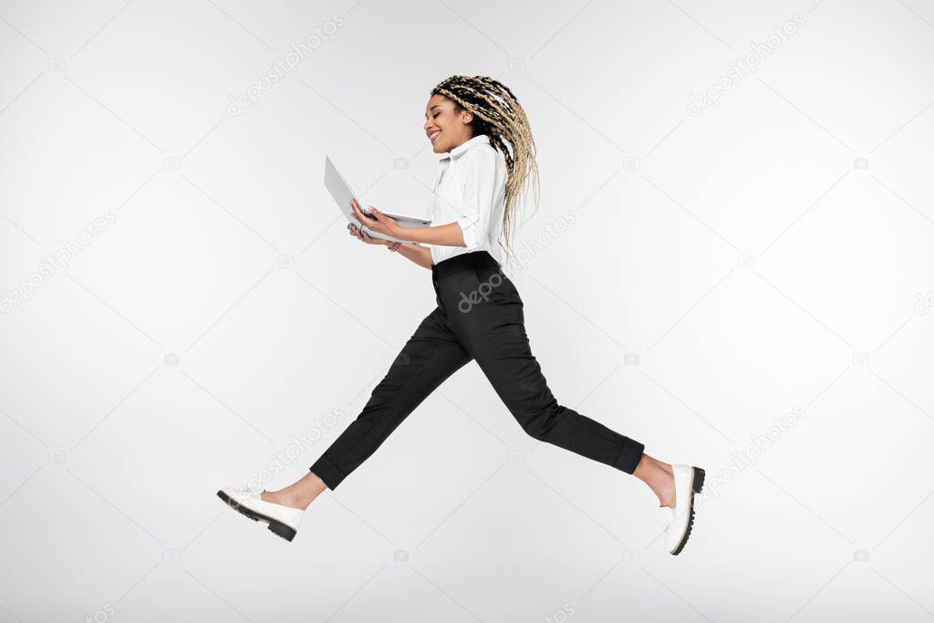 smiling african american businesswoman levitating with computer isolated on white