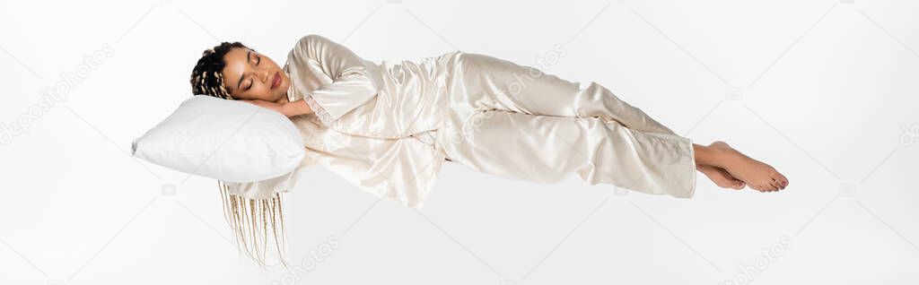 young african american woman in silk pajamas levitating in sleep isolated on white, banner