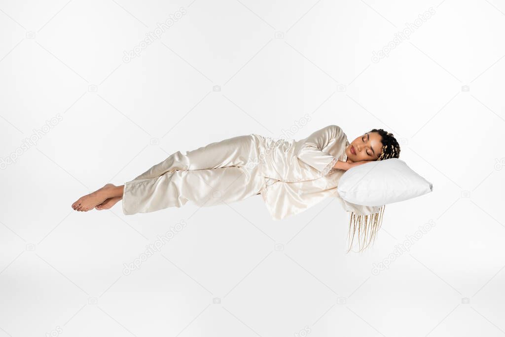 barefoot african american woman in silk pajamas sleeping in air isolated on white