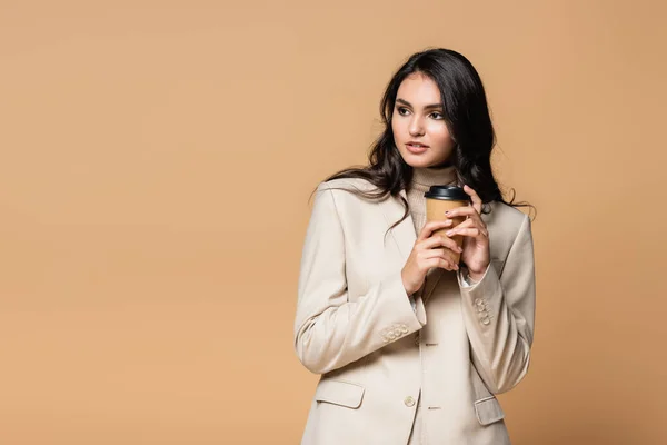 young pretty model in turtleneck holding paper cup isolated on beige