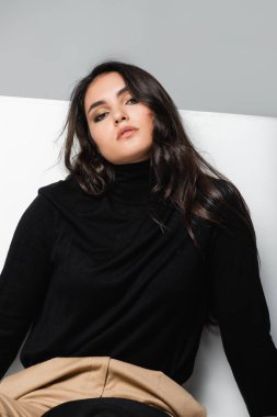 Beyaz kübün yakınındaki kameraya bakan siyah balıkçı yakalı şık model gri üzerinde izole edilmiş. 