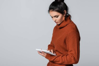 Gri üzerine izole edilmiş dijital tablet kullanan örgü kazaklı genç bir kadın. 