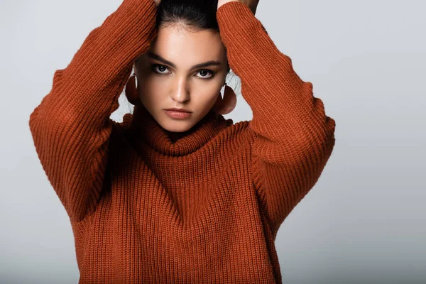 model in earrings and knitted sweater looking at camera isolated on grey
