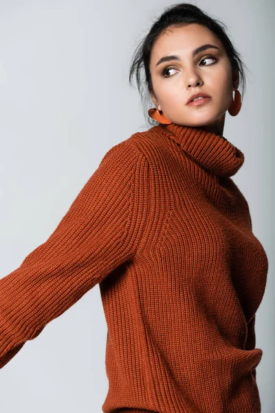 young woman in earrings and knitted sweater isolated on grey