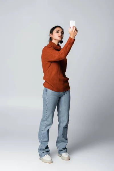 Junge Frau Pullover Und Jeans Blickt Auf Smartphone Grau — Stockfoto