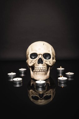burning candles near spooky skull on black  clipart