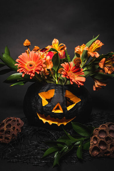 orange flowers with green leaves in spooky and carved pumpkin on black background 