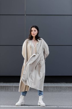 Bej ceketli, beyaz deri çizmeli, modaya uygun bir kadın elleri arkada duruyor.