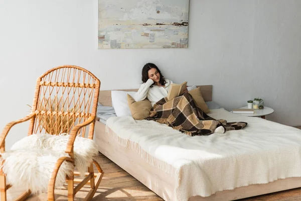 Brunette Woman Reading Book Bed Plaid Blanket Wicker Chair — Stock Photo, Image