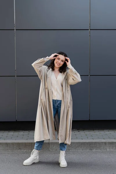 Mujer Sonriente Impermeable Largo Botas Blancas Ajustando Pelo Cerca Pared — Foto de Stock