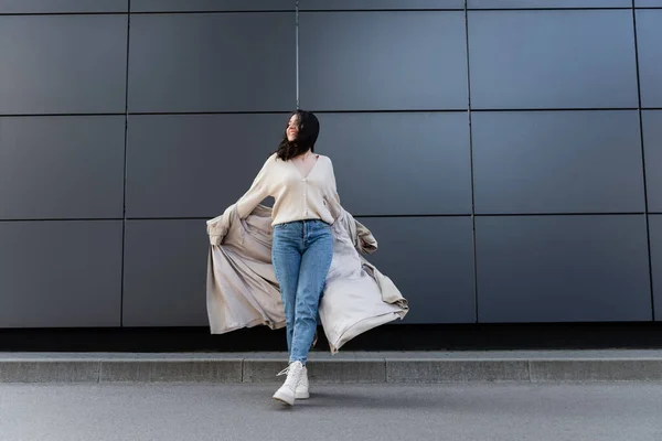 Veselá Žena Džínách Bílé Boty Pózující Pláštěnkou Poblíž Šedé Zdi — Stock fotografie