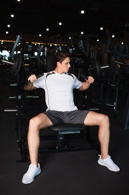 Kol genişletme egzersiz makinesindeki sporcu eğitiminin tam uzunluk görünümü oturma konumunda