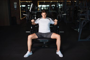Spor salonunda kol genişletme egzersizi yapan sporcunun tam boy görüntüsü.