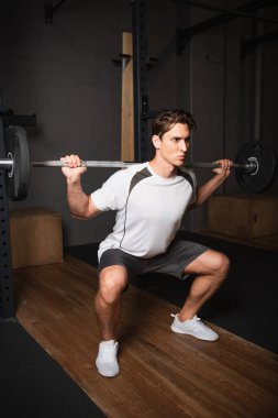 Spor giyimli bir adam spor merkezinde halterle mekik çekiyor.