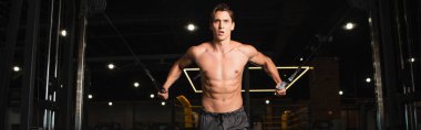 Spor salonunda spor yapan üstsüz atletik adam spor salonunda kablo egzersiz makinesi çekiyor.