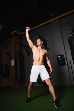 Spor salonunda kettlebell ile spor yapan üstsüz kaslı sporcunun tam boy görüntüsü.