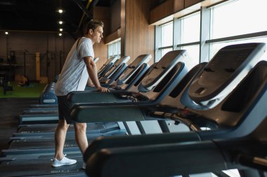 Spor salonundaki koşu bandında duran sportif adamın tam boy görüntüsü.