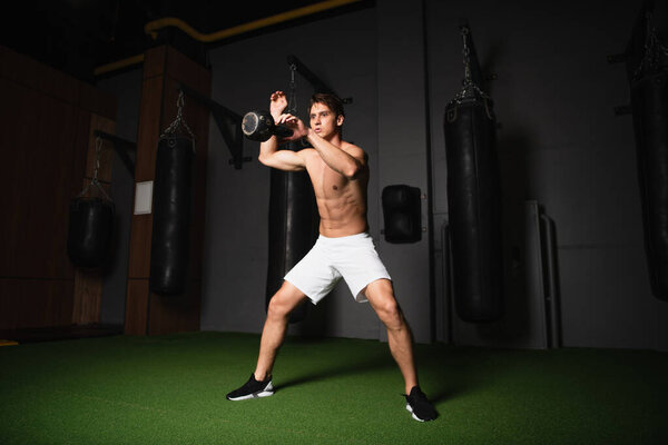 full length view of shirtless athletic man juggling with kettlebell while training in gym
