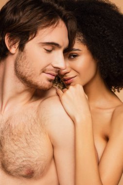 Seksi İspanyol kadın kameraya gülümserken bej renkli bir erkeğin omzuna yaslanıyor.