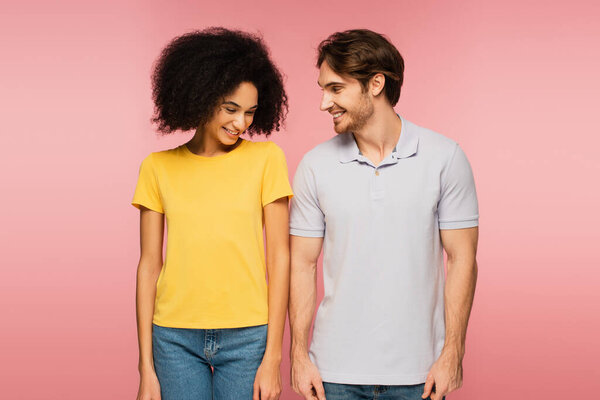 pretty latin woman and young man smiling while standing isolated on pink