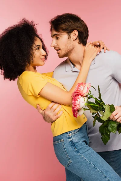 Young Man Fresh Roses Embracing Pleased Latin Girlfriend Isolated Pink — Stock Photo, Image