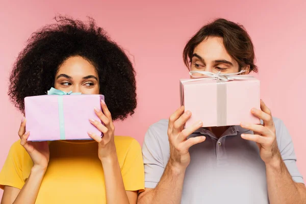 Pareja Multiétnica Positiva Oscureciendo Caras Con Cajas Regalo Aisladas Rosa — Foto de Stock