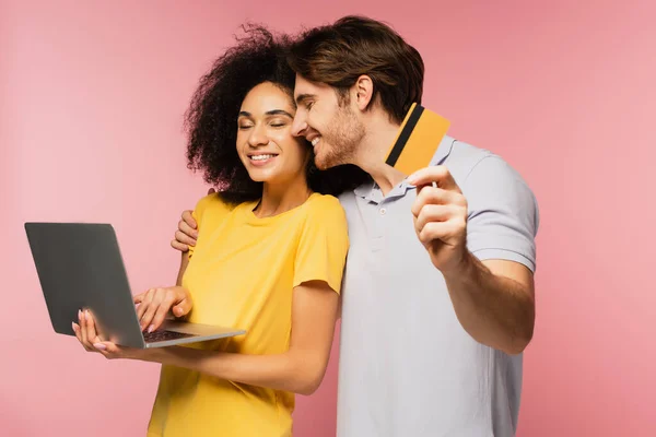 快乐的男人拿着信用卡 用粉红色的笔记本电脑拥抱着快乐而惊慌的女朋友 — 图库照片
