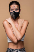 žena s tygřím make-upem a ochrannou maskou pózující izolovaně na béžové