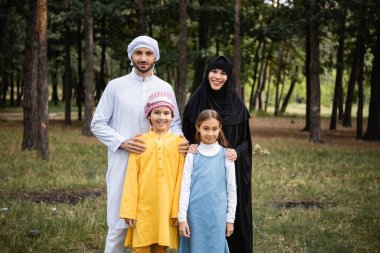 Gülümseyen Arap aileler çocukları kucaklıyor ve parkta kameraya bakıyor. 