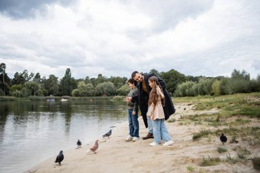 Muslim father pointing at lake near kids and birds in park  clipart