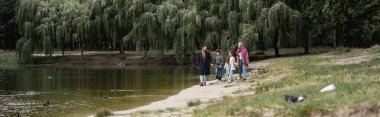 Muslim family walking near lake in park, banner  clipart